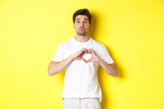 Cute guy pucker lips and waiting for kiss, showing heart gesture. Concept of love and romance.