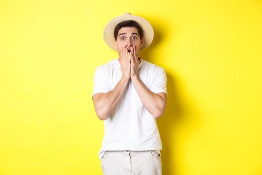 Concept of tourism and summer. Shocked guy jumping from fear, standing startled against yellow background.