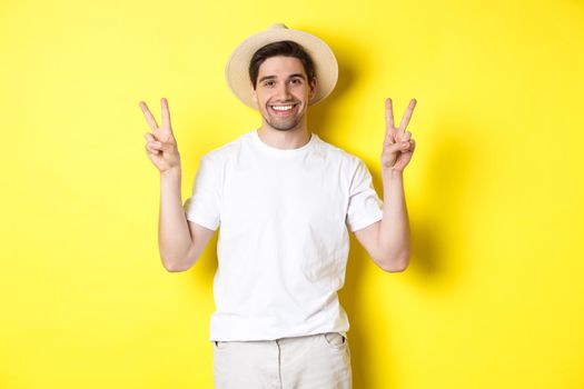 Concept of tourism and vacation. Happy male tourist posing for photo with peace signs, smiling excited, standing against yellow background.