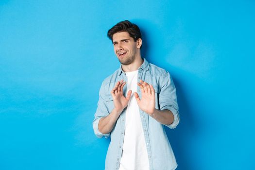 Displeased man refusing, saying no and cringe from something disgusting, standing over blue background.