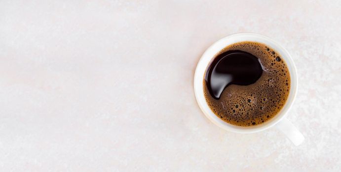 Freshly brewed coffee with foam in a white cup on a light background, top view. Morning invigorating drink. Banner, place for text and advertising.