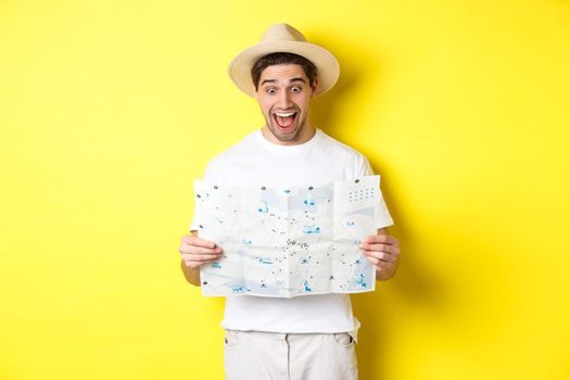 Travelling, vacation and tourism concept. Man tourist looking happy at map with sighsteeings, explore city, standing over yellow background.