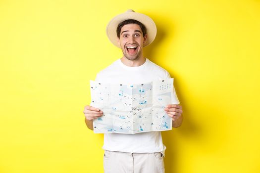 Travelling, vacation and tourism concept. Excited man tourist going sightseeing with map, standing over yellow background.