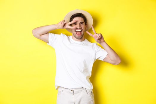 Concept of tourism and vacation. Happy man tourist posing for photo with peace signs, smiling excited, standing against yellow background.