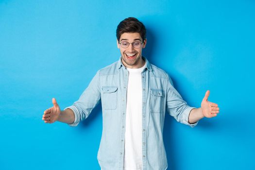 Excited handsome man showing big size object and looking amazed, standing over blue background.
