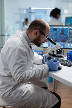 Biologist scientist man doctor examining coronavirus sample results using medical microscope developing virus vaccine. Biochemistry investigation in scientific hospital laboratory. Biomedical industry