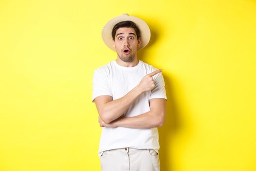 Surprised man in straw hat pointing finger right, showing promo banner, standing over yellow background. Copy space