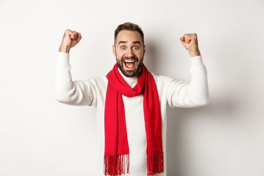 Christmas holidays and New Year concept. Excited man rejoicing, winning prize, raising hands up and looking relieved, triumphing, standing over white background.