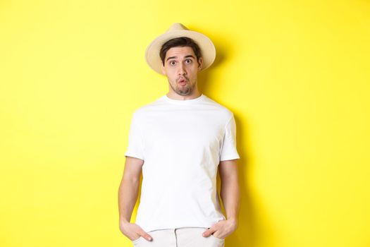 Confused guy traveller in straw hat looking puzzled, stare at camera, standing over yellow background. Copy space