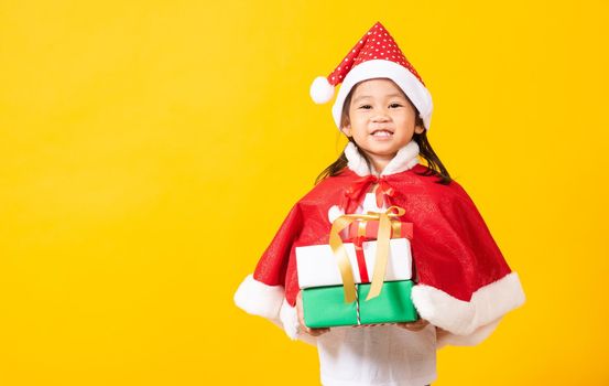 Asian little cute girl smile and excited, Kid dressed in red Santa Claus hat hold gift box on hands concept of holiday Christmas Xmas day or Happy new year, studio shot isolated on yellow background