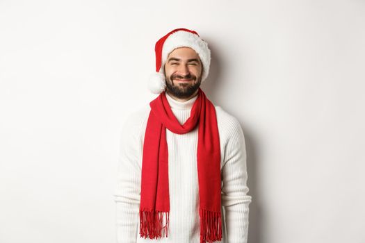 Christmas holidays. Bearded man in santa hat and red scarf looking happy, enjoying New Year party celebration, standing over white background.