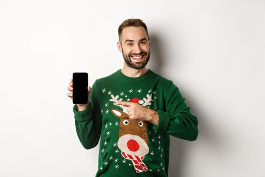 New Year, holidays and celebration. Handsome man smiling, pointing finger at mobile screen, showing app, standing over white background.