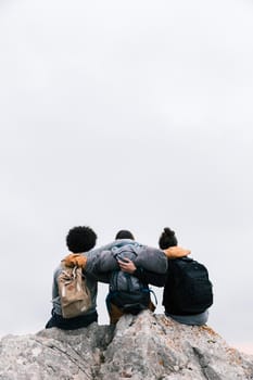 three friends with their arms around sitting top mountain. High resolution photo