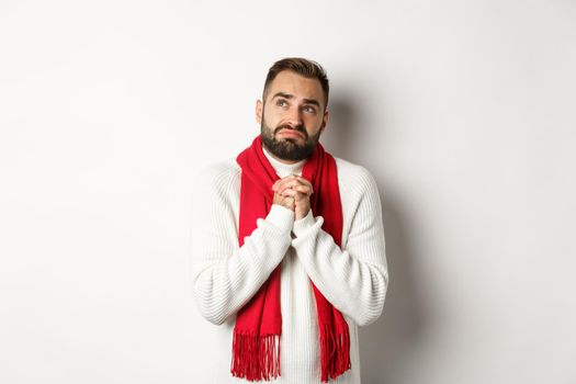 Christmas holidays and New Year concept. Sad and miserable man praying to God, making with and holding hands in pray, looking up at sky and begging, standing over white background.