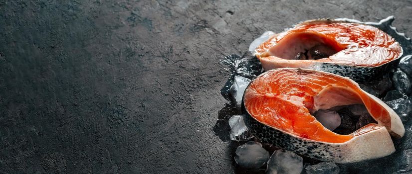 Two raw wild salmon steaks on ice over black textured background. Salmon steaks with copy space left. Long horizontal banner
