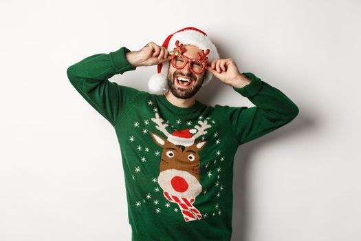 Christmas holidays, celebration concept. Happy man in Santa hat and funny party glasses standing against white background.