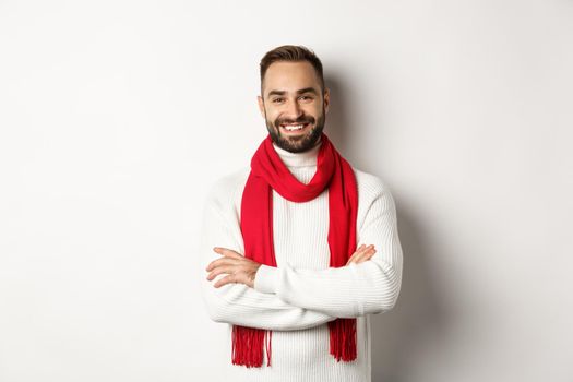 Christmas holidays and celebration concept. Handsome bearded man in sweater celebrating new year, wearing red scarf and smiling, standing over white background.