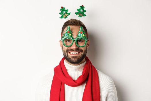 Christmas, New Year and celebration concept. Close-up of handsome bearded man in funny party glasses looking happy, standing against white background.