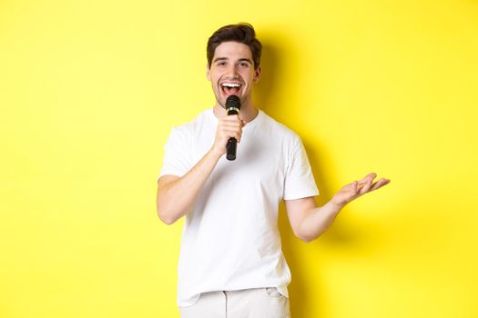 Happy man entertainer performing, talking in microphone, making speech or stand-up show, standing over yellow background.
