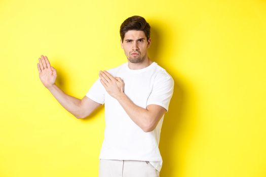 Man showing kung-fu skills, martial arts ninja movement, standing in white t-shirt ready to fight, standing over yellow background. Copy space