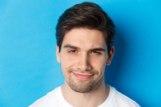 Headshot of thoughtful handsome man, looking intrigued and squinting, thinking about something, standing over blue background.