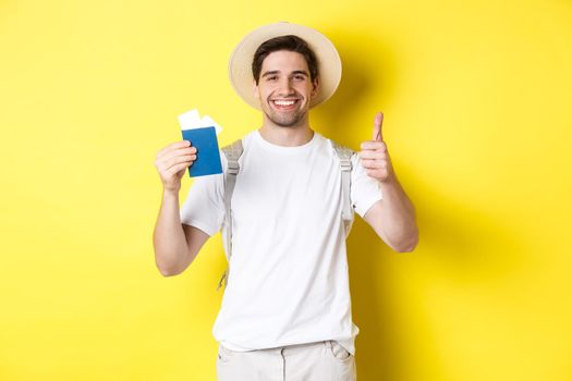 Tourism and vacation. Satisfied male tourist showing passport with tickets and thumb up, recommending travel company, standing over yellow background.