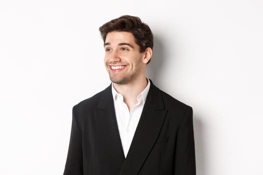 Close-up of handsome male entrepreneur in suit, looking left and smiling, standing against white background.