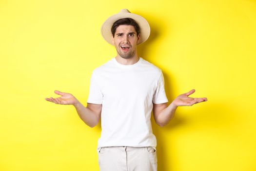 Concept of tourism and summer. Confused guy traveller shrugging, cant understand something, standing against yellow background.