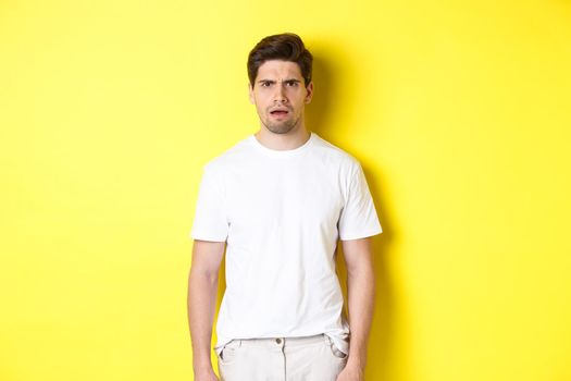 Image of confused and puzzled man cant understand something, frowning and looking shocked, standing over yellow background.