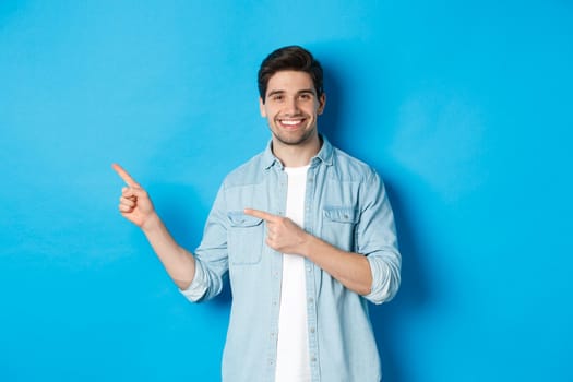 Handsome caucasian man in casual outfit, pointing fingers left and smiling, showing promo offer, standing over blue background.