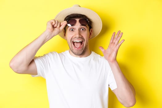Concept of tourism and holidays. Excited man tourist take-off sunglasses and looking amazed at promo offer, standing over yellow background.