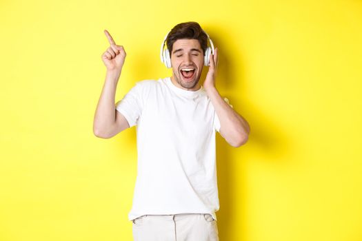 Happy man listening music in headphones, pointing finger at promo offer for black friday, standing over yellow background.