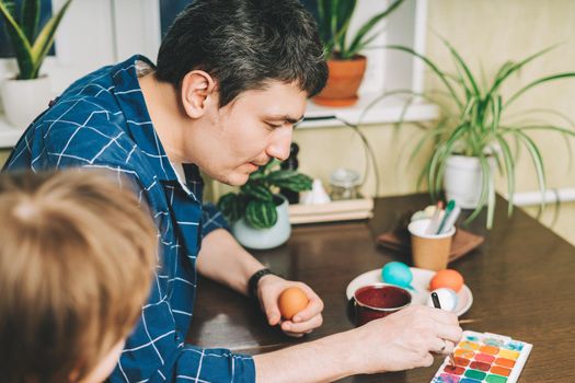 Easter day. Father and son painting eggs on wooden background. Family sitting in a kitchen. Preparing for Easter, creative homemade decoration.