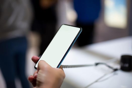 a caucasian man holds new smartphone with white screen copyspace. close up, soft focus. background in blur