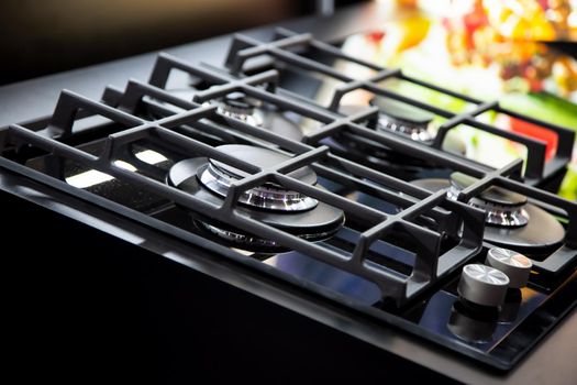 New modern black gas stove with four burners for the kitchen, stainless steel surface. Cast iron grates. yellow background in blur