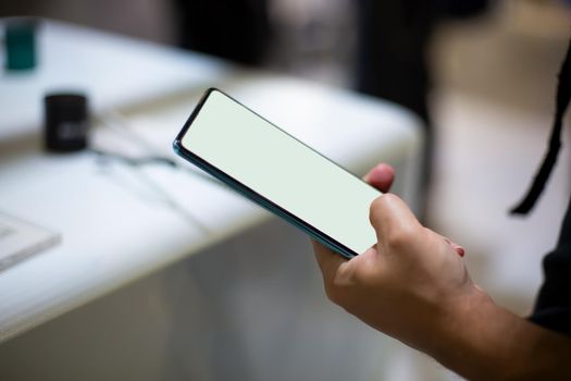 a caucasian man holds new smartphone with white screen copyspace. close up, soft focus. background in blur