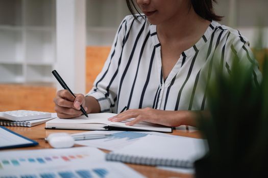 Close up of businessman or accountant hand holding pen working on calculator and laptop computer to calculate business data during make note at notepad, accountancy document at office.