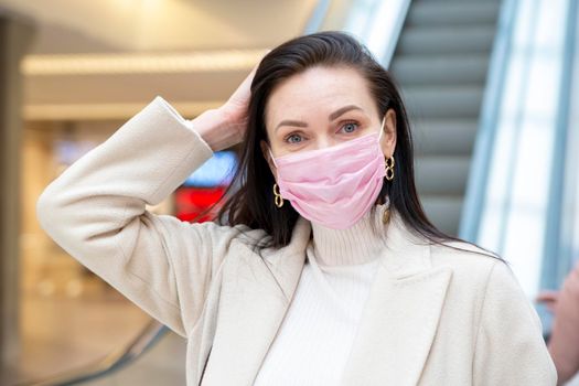 beautiful woman in a pink medical mask on her face against the background of the escadator in a public place.