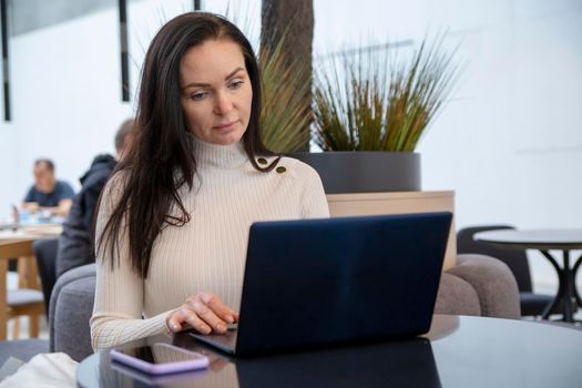 young woman with protective face mask works on laptop in cafe.