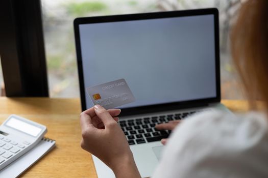 Young woman holding credit card and using laptop computer. Businesswoman working at home. Online shopping, e-commerce, internet banking, spending money, working from home concept