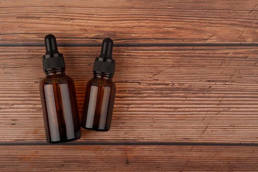 Two dark transparent glass bottles with skin serum or oil for manicure on dark wooden background with copy space. Concept of organic natural skin care products and beauty serums