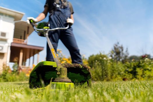 A young man is actively mowing a lawn in his beautiful green summer garden, bottom view. A professional gardener with a lawnmower cares for the grass in the backyard.