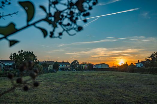 Rural landscape with beautiful gradient evening sky at sunset. Green field and village on horizon