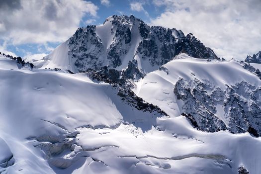 Harsh majestic landscape with snow-capped mountains, glacier and ice cracks covered with snow on a sunny day.