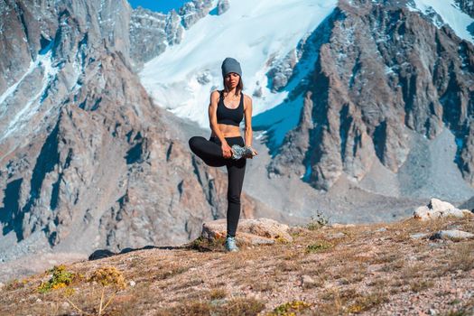 A young sports girl practices yoga on a background of snow-capped mountains on a sunny day, a woman does exercises, trains and meditates in a picturesque mountainous area.