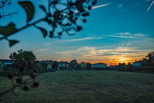 Rural landscape with beautiful gradient evening sky at sunset. Green field and village on horizon