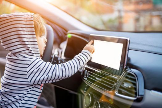 curious toddler girl holding, touching, and turning a car mnultiedia touch screen player button. empty white screen