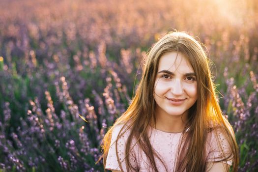 Beautiful woman is posing at field of purple lavender flowers. Beautiful woman in the lavender field on sunset in France .Girl collect lavender. Soft focus.