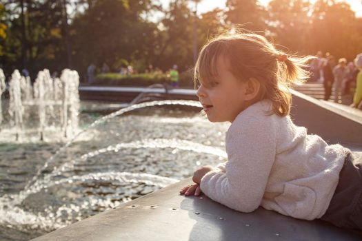 adorable toddler girl looks at the fountains in the park in the park on a sunny day.