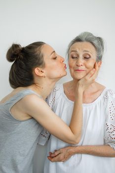 Happy senior mother is hugging her adult daughter, the women are laughing together, sincere family of different age generations having fun on white background, mothers day